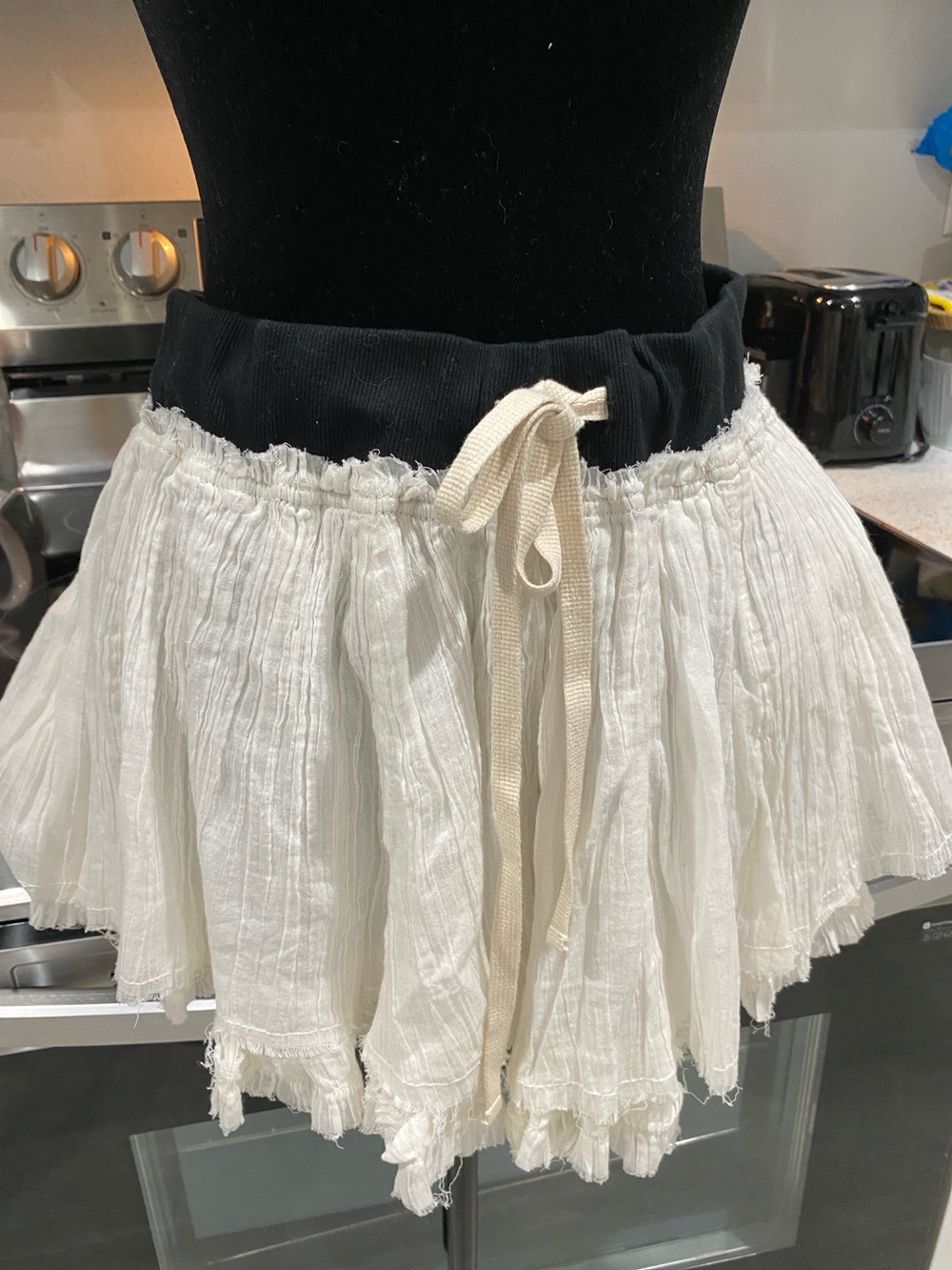 “Free Est” white gauze layered mini skirt. Black band w beige tie, raw edging